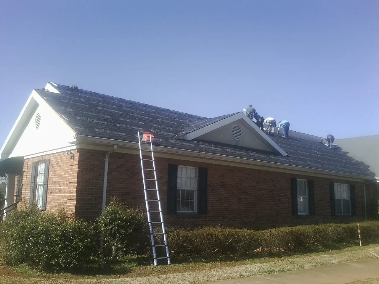 Crew tearing shingles off a brick ranch roof with a ladder set — Metal Roof Repair work by our crew in Pike