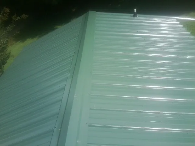 New green metal panels meeting at the ridge of a roof — Flat Roof Repair work by our crew in Pike