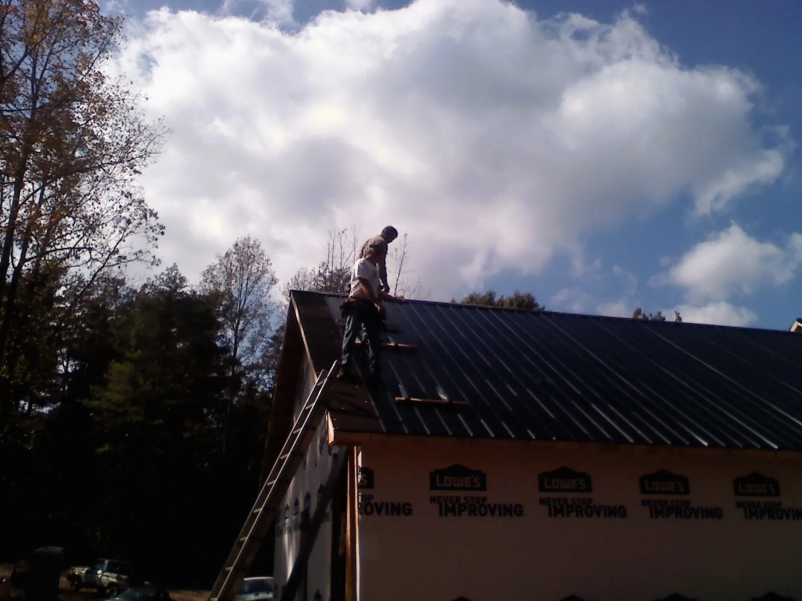 Roofer fastening dark metal panels high against a cloudy sky, from a Roof Inspection job in Pike