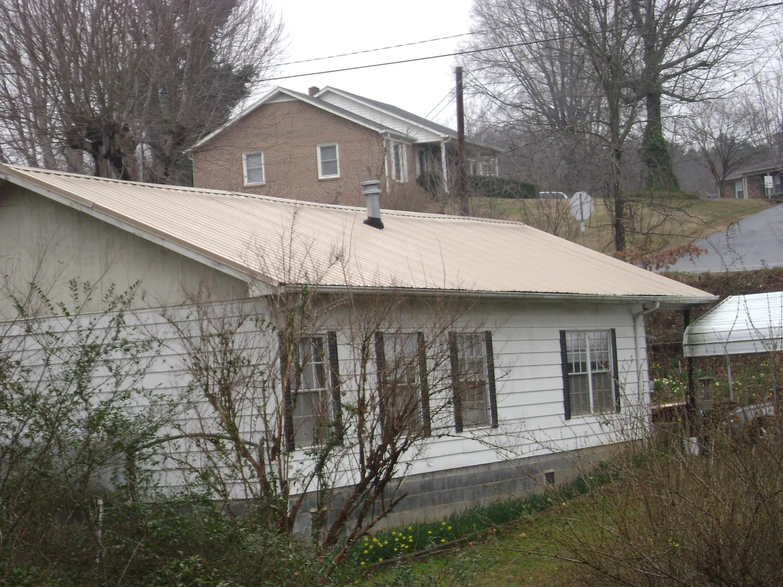 Tan metal roof on a white sided house set into a hillside — Commercial Roofing by Roofing Brothers in Pike